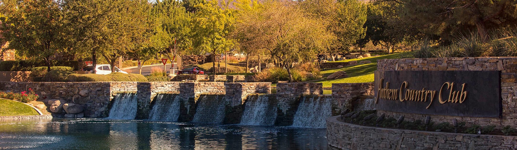 Brick stand with sign that says Anthem Country Club, mini waterfalls into a lake with golf course trees and bushes.