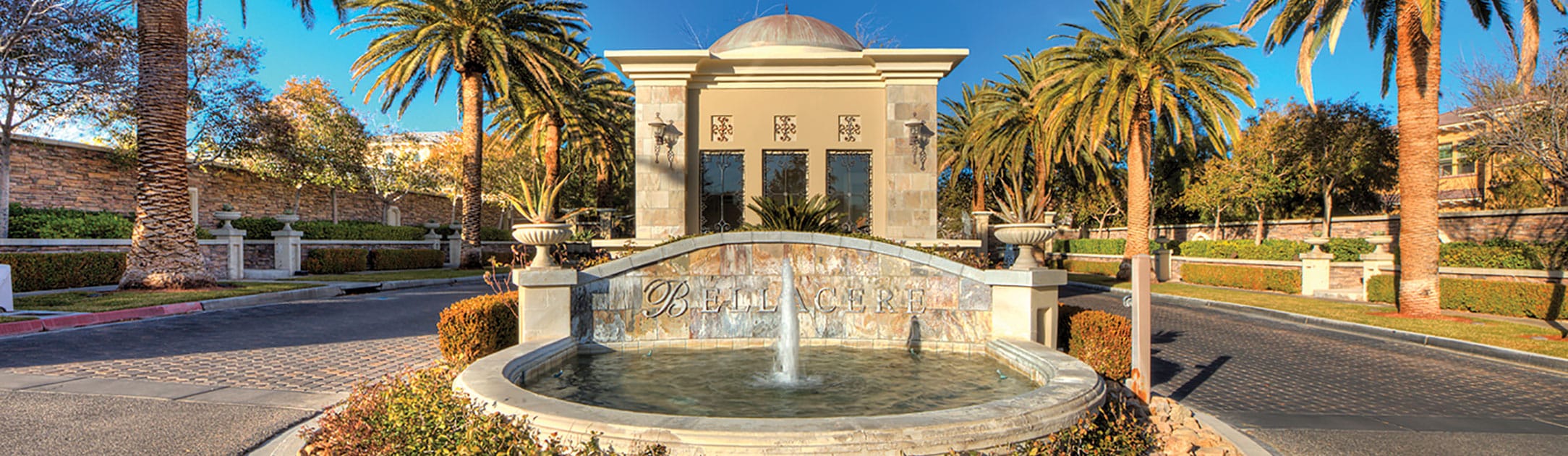 Fountain with the sign Bellacere, gate entrance in the back with palm trees.