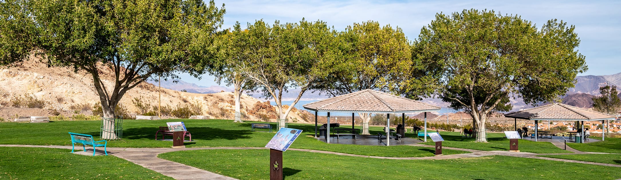 Park with tress, a bench, stand with information to read and gazebo.