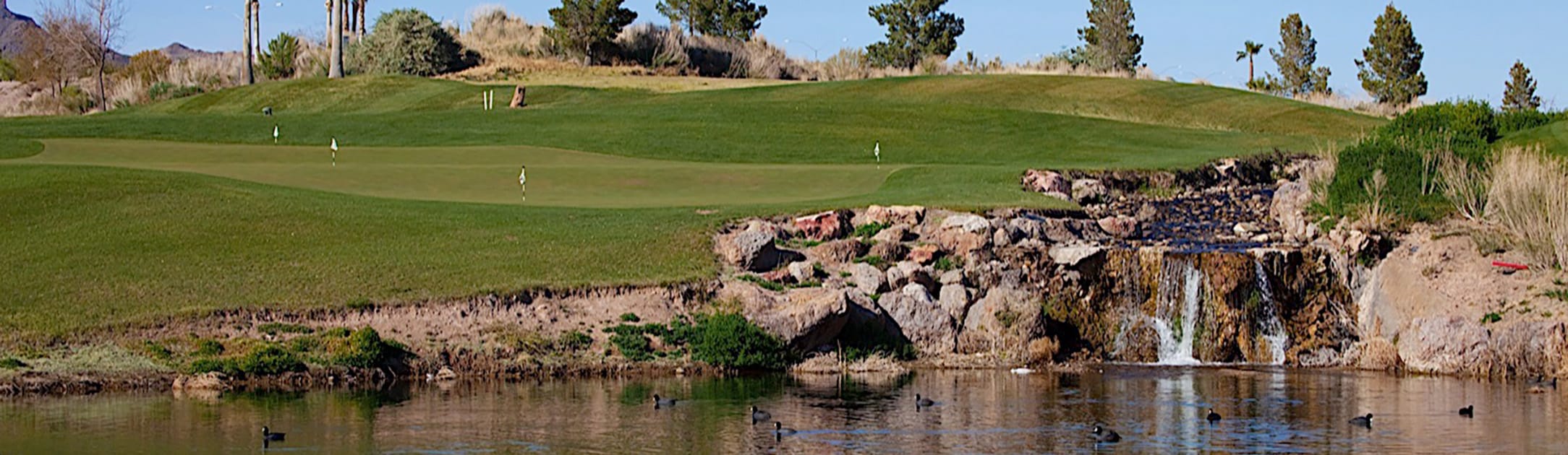 Golf course with trees and rock waterfalls into a lake.