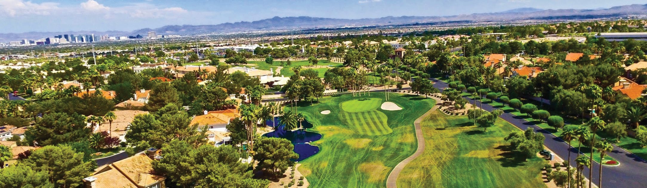 Golf Course with luxury homes around it. High rise skyline and mountains in the background.