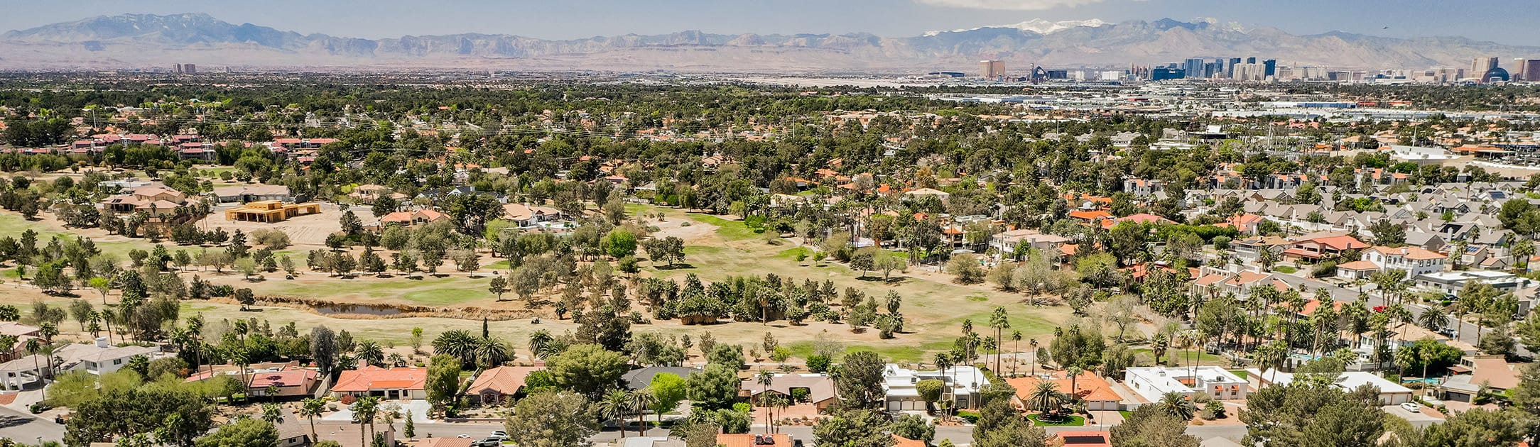 Aerial view of golf course and neighborhood with high rises and mountains in the background.