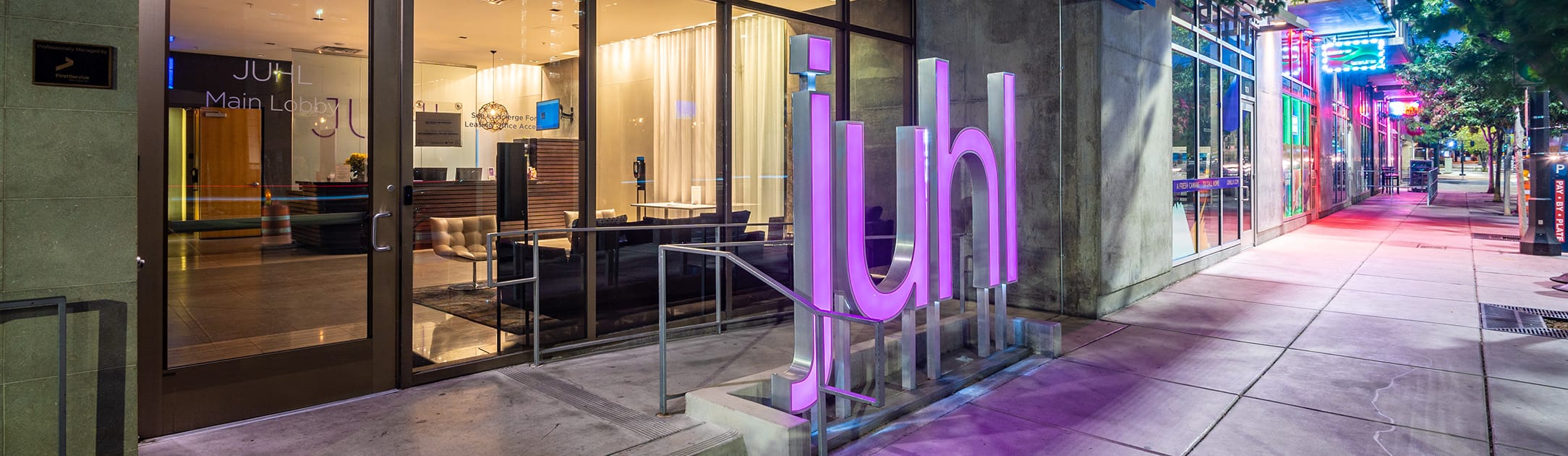 Sidewalk with a purple Juhl sign and entrance to the high rise.
