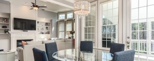 Round glass kitchen table with blue chairs, chandelier and windows