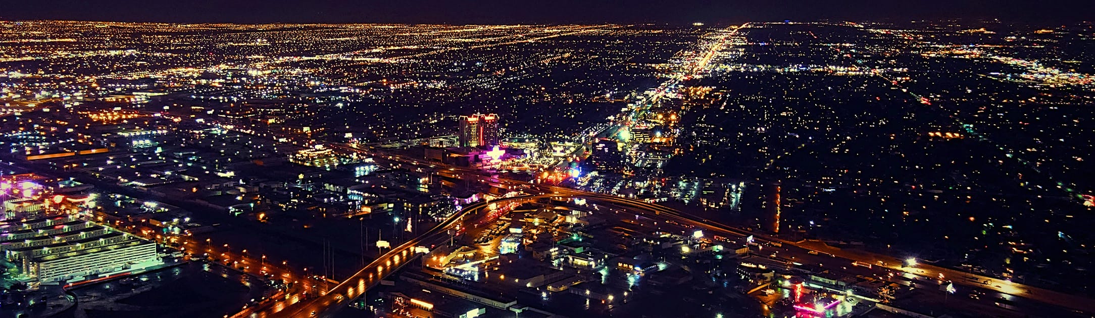 Night time high aerial view of neighborhood. Main streets and freeways have lots of lights and homes with lights on.