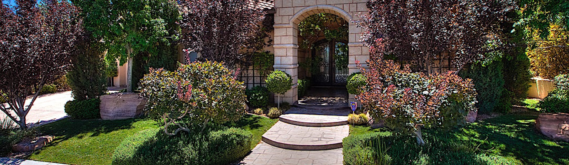 Front view of a home with an arched brick entrance, grass, bushes, trees and ivy on the walls.