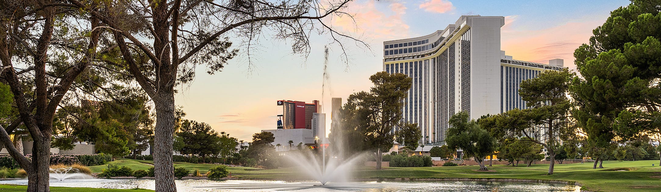 Golf course with a fountain and trees. A high rise tower to the right and another high rise tower in the middle background with text that says Conrad.