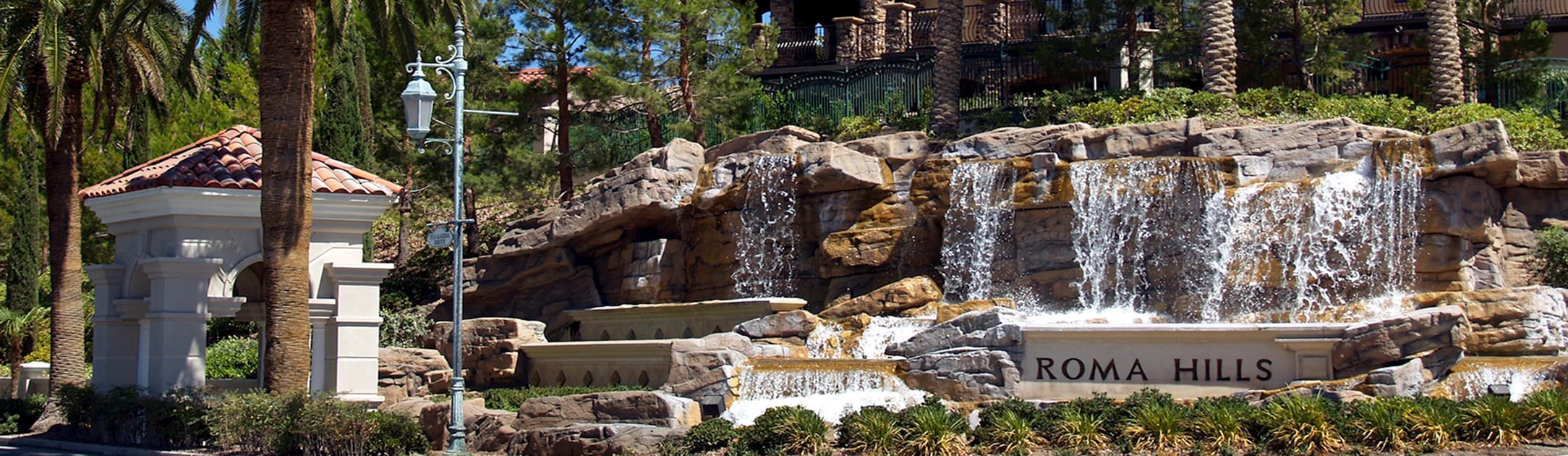Rocks and waterfalls with a sign that says Roma Hills and gate entrance building to the left of it.