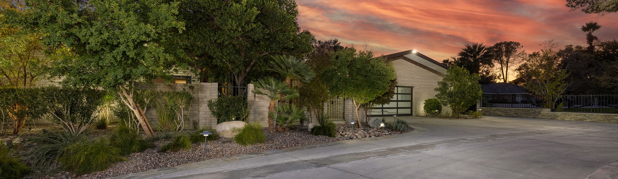 front of house with bushes, tress and orange sunset in the background.