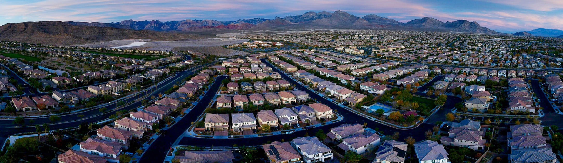 Aerial view of neighborhood at dusk with red rock mountains in the background.