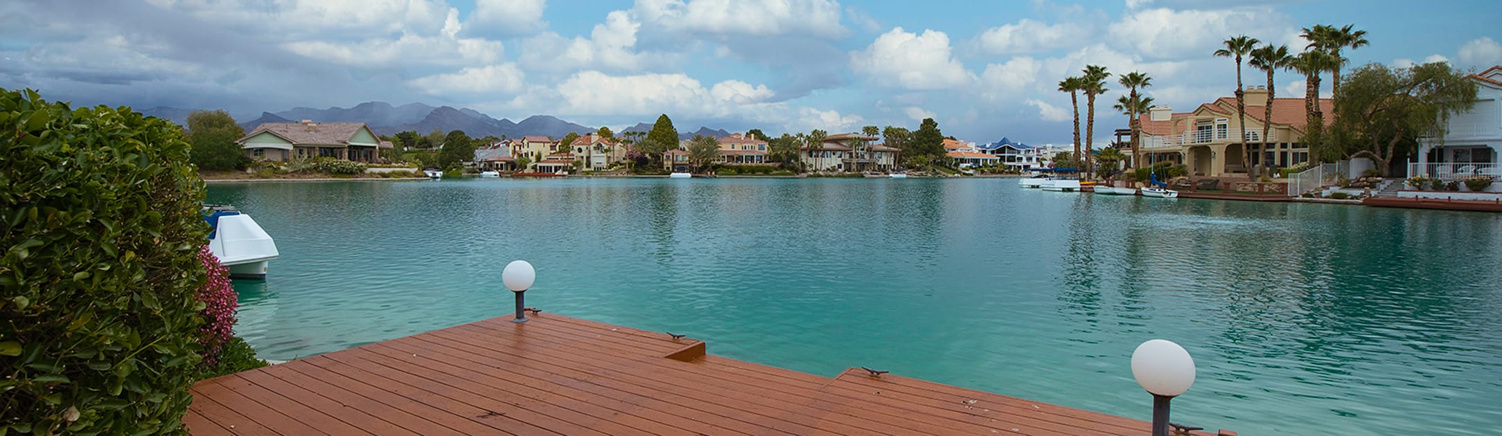 View from boat dock of a lake with luxury homes and palm trees.