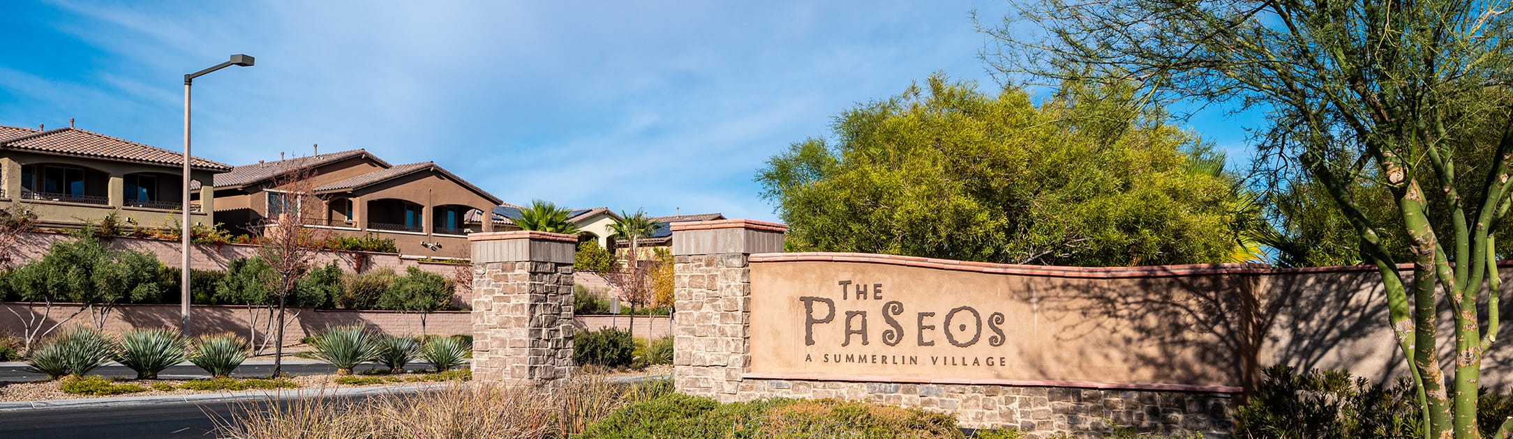 Brick stand with sign that says The Paseos a Summerlin Village, trees and homes in the background.