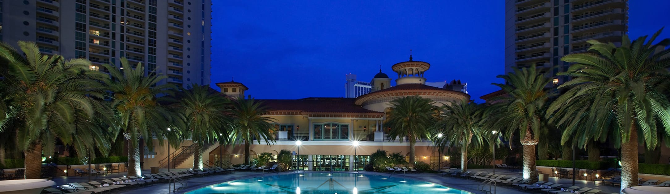 Night view of pool and club house with towers on the left and right.