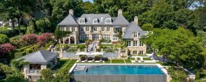 Back of a luxury 3 story home with a pool, grass and trees