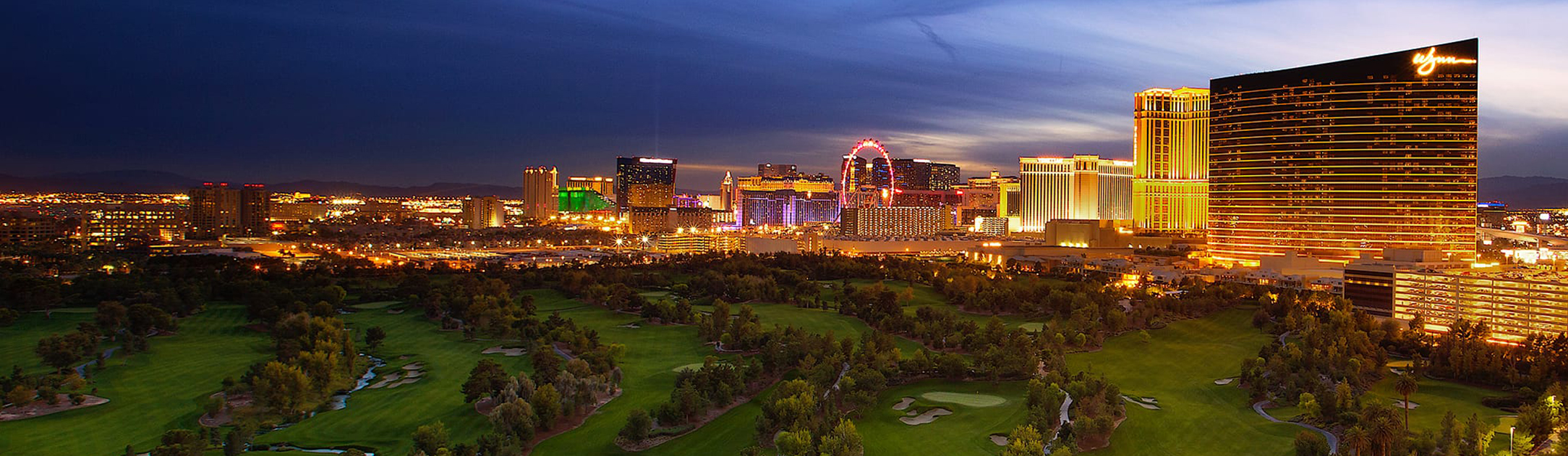 Night time aerial view of golf course with hotels, casinos and high rises behind it.