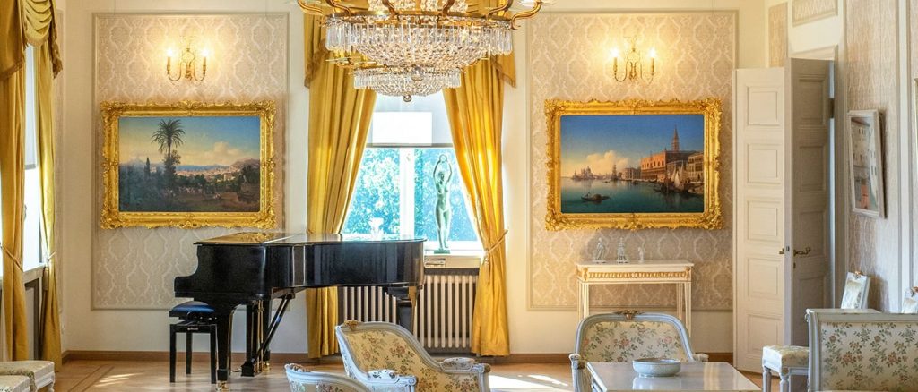 Luxury room with a piano, exquisite chandelier, gold framed paintings and gold embroidered chairs.