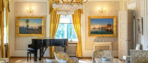 Luxury room with a piano, exquisite chandelier, gold framed paintings and gold embroidered chairs.