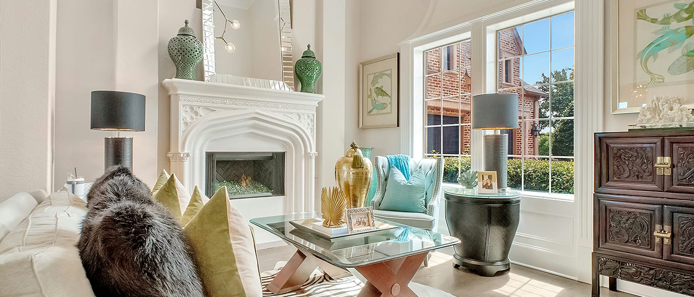 Living room with fireplace and mantel with mirror and candles on top. Windows with a view and couch and chair with colorful pillows.