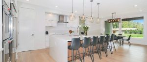 Kitchen with island and black chairs, white cabinetry, windows.