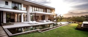 Back of Luxury home with deck, pool, green grass and sunny day.